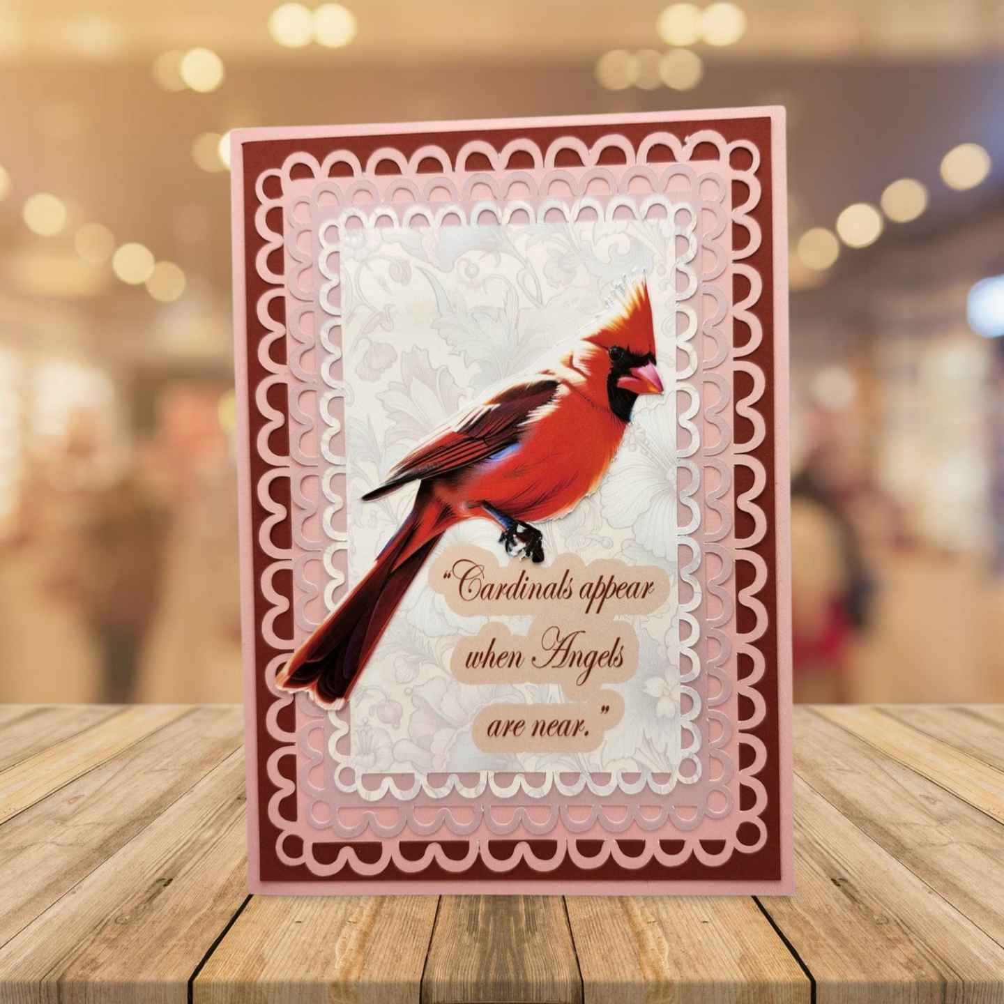 Card with red cardinal bird and text on a wooden surface with blurred background