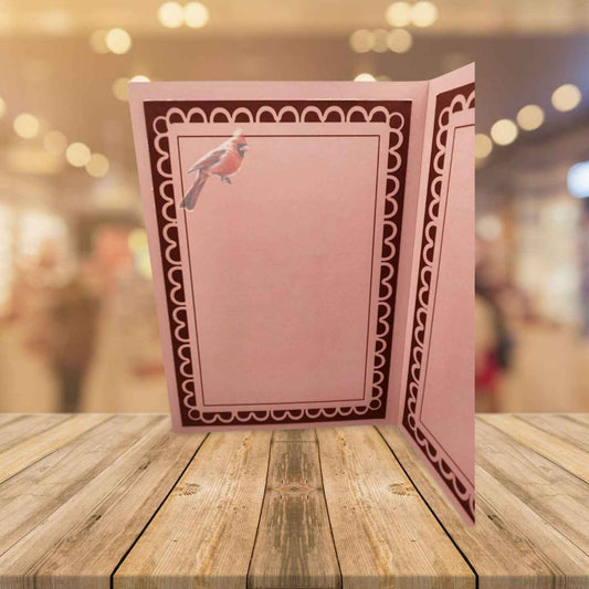 Pink card with decorative border and bird illustration on a wooden surface with blurred background