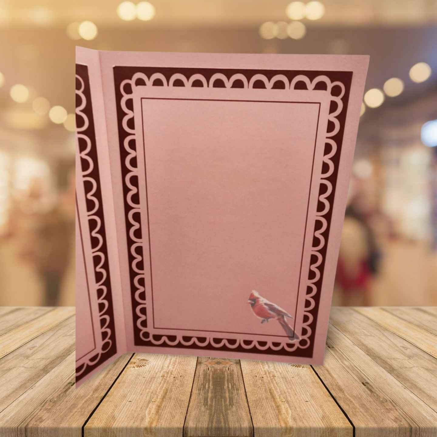 Pink greeting card with decorative border and bird illustration on a wooden surface.