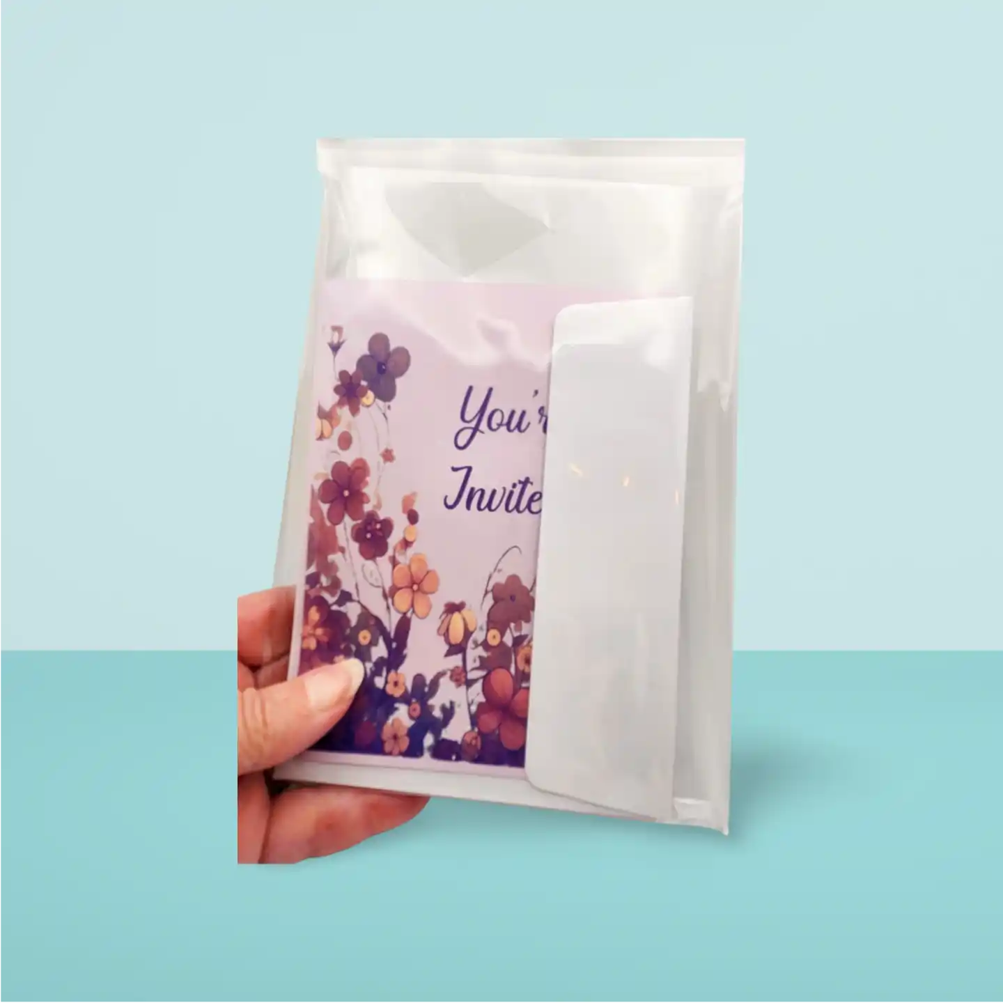 Floral invitation card in a clear plastic sleeve held by a hand on a light blue background