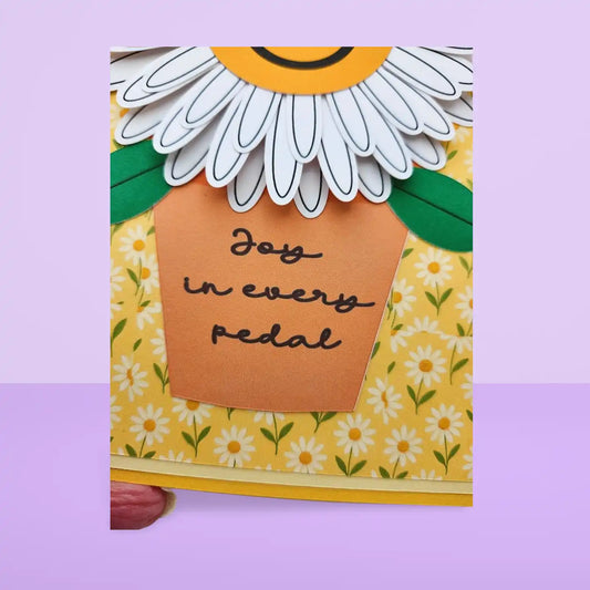 Card with a daisy design and 'Joy in every pedal' text on a yellow background