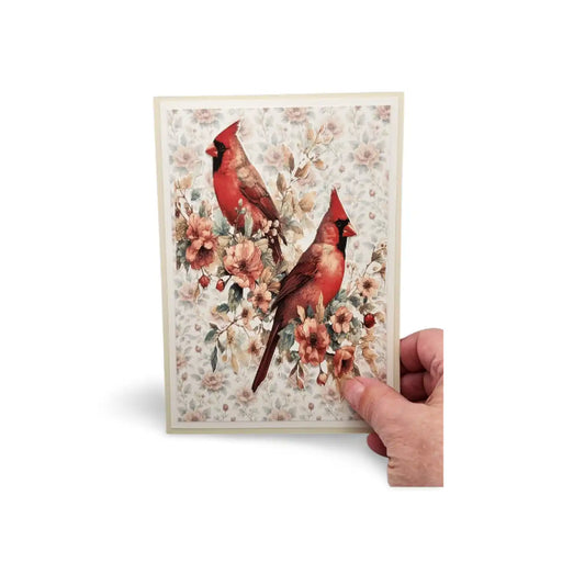 Card with two red cardinals and floral design held by a hand on a white background