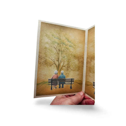 Greeting card with an illustration of two people on a bench under a tree, held by a hand.