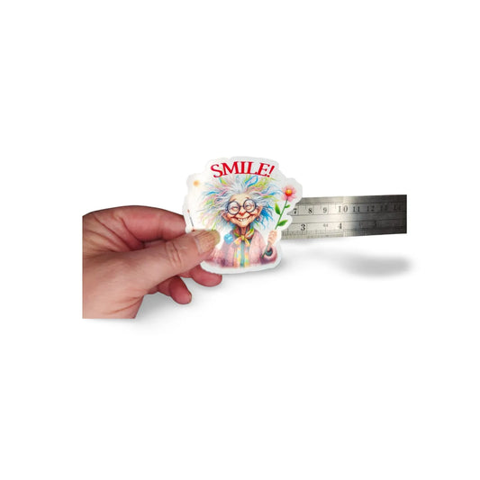 Colorful sticker with a cartoon character and 'SMILE!' text held by a hand, with a ruler for scale on a white background.