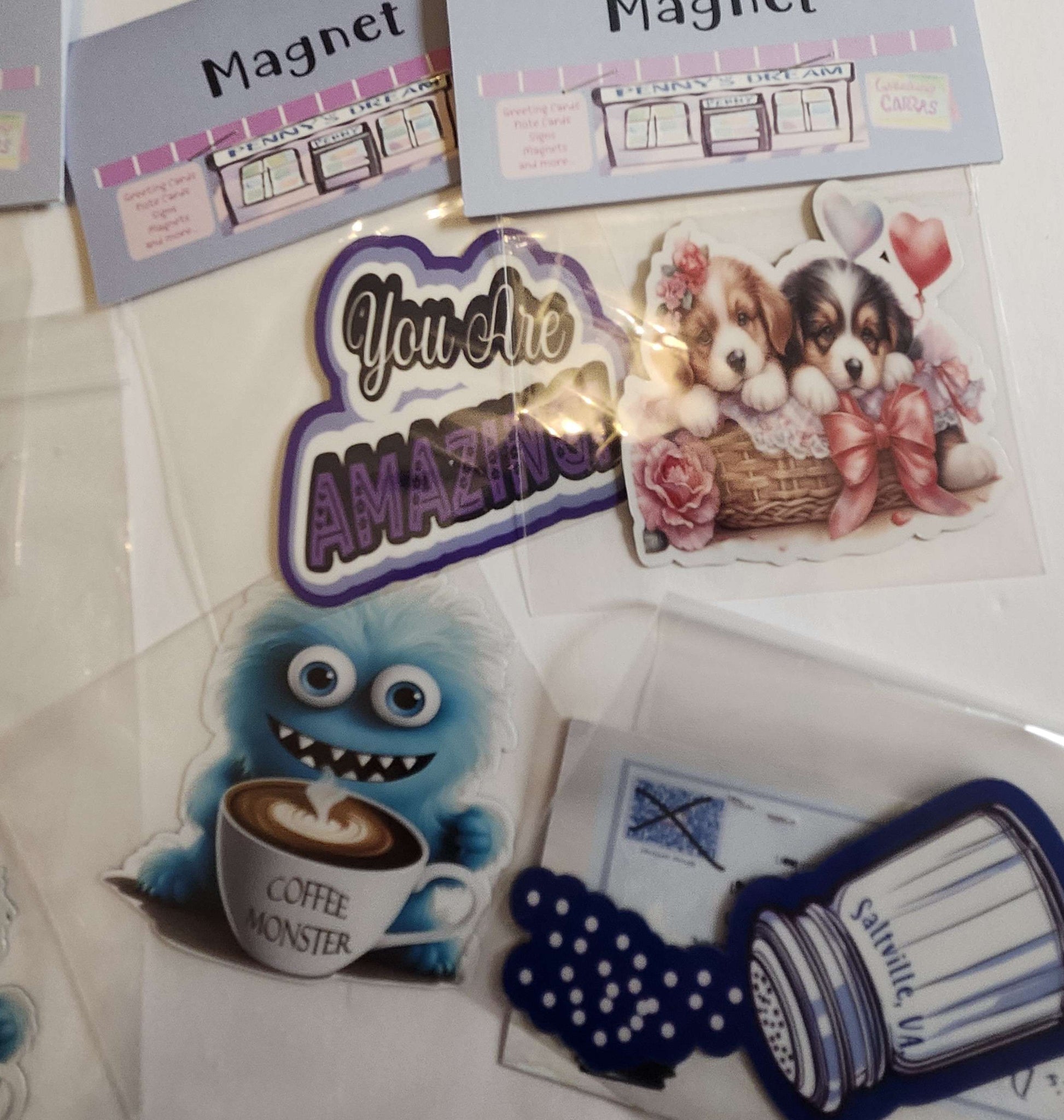 Collection of decorative magnets including a coffee monster, puppies with bows, and 'You are Amazing' text.