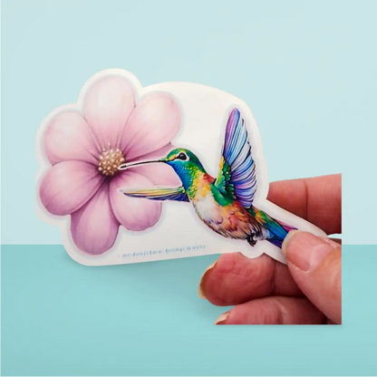 Sticker of a colorful hummingbird and pink flower held by a hand on a light blue background