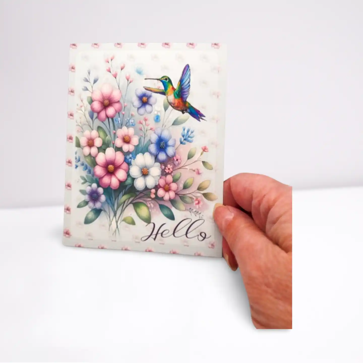 Hand holding a card with floral design and 'Hello' text on a white background