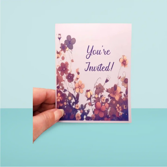 Hand holding a floral invitation card with 'You're Invited!' text on a light blue background