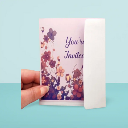 Hand holding a floral invitation card with 'You're Invited' text on a light blue background