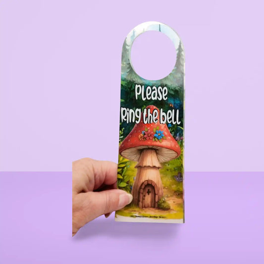 Door hanger with mushroom house design and text 'Please Ring the Bell' held against a purple background
