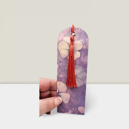 Decorative bookmark with floral design and red tassel held by a hand on a light gray background
