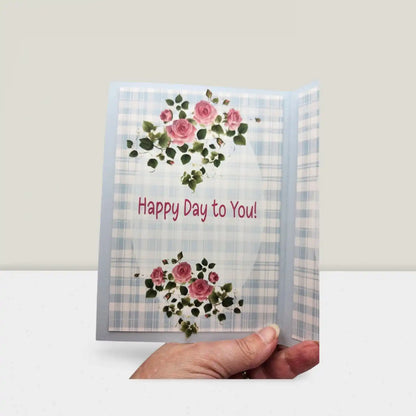 Greeting card with floral design and 'Happy Day to You!' text held by a hand on a white background