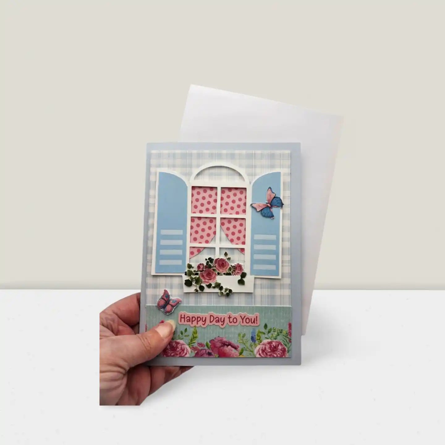 Handmade card with floral design and 'Happy Day to You!' text held by a hand on a white background