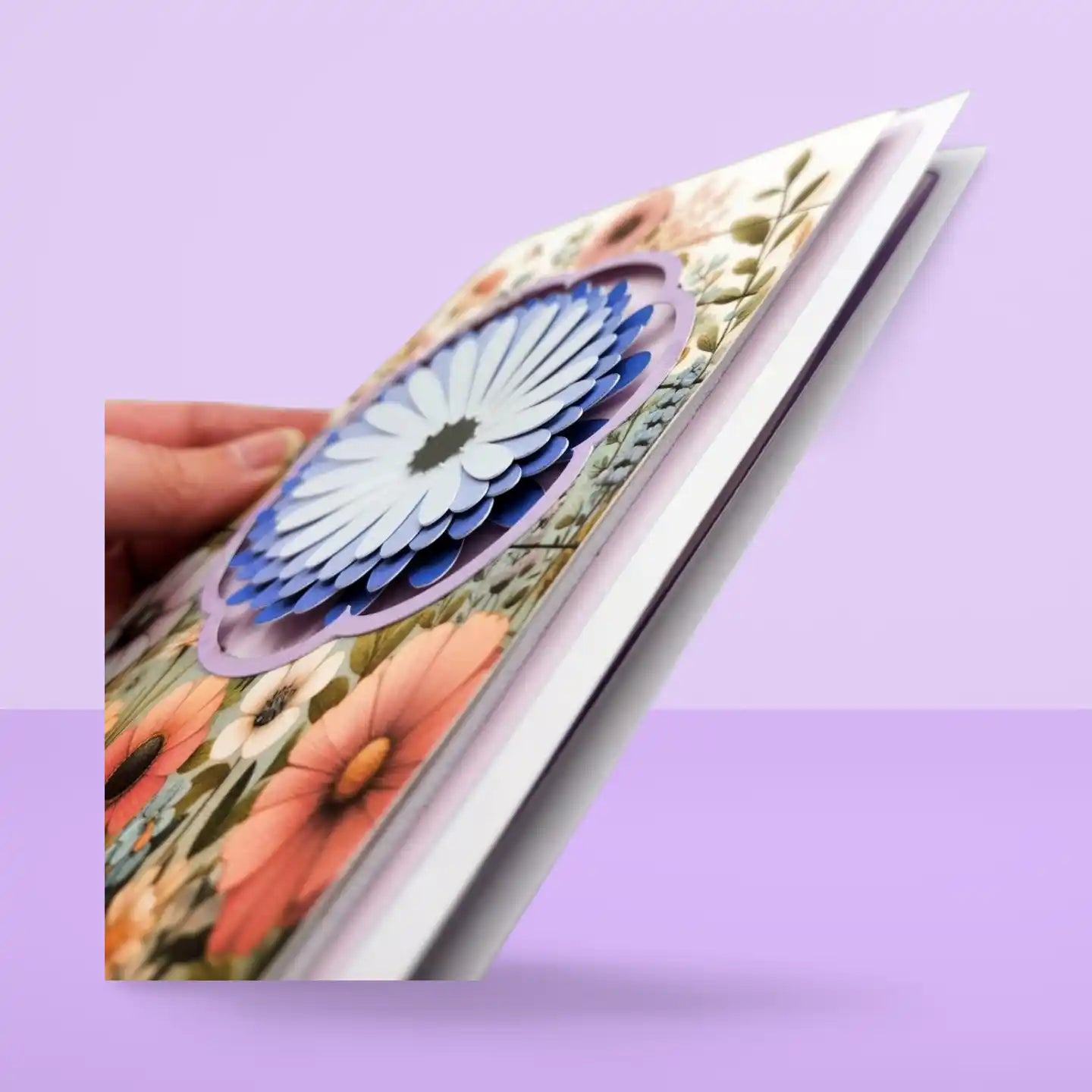 Floral card with a hand holding it against a purple background
