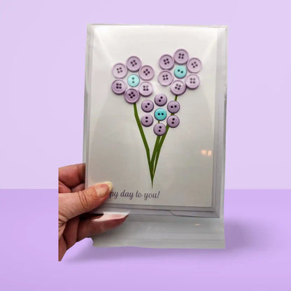 Card with button flower design held by a hand on a purple background