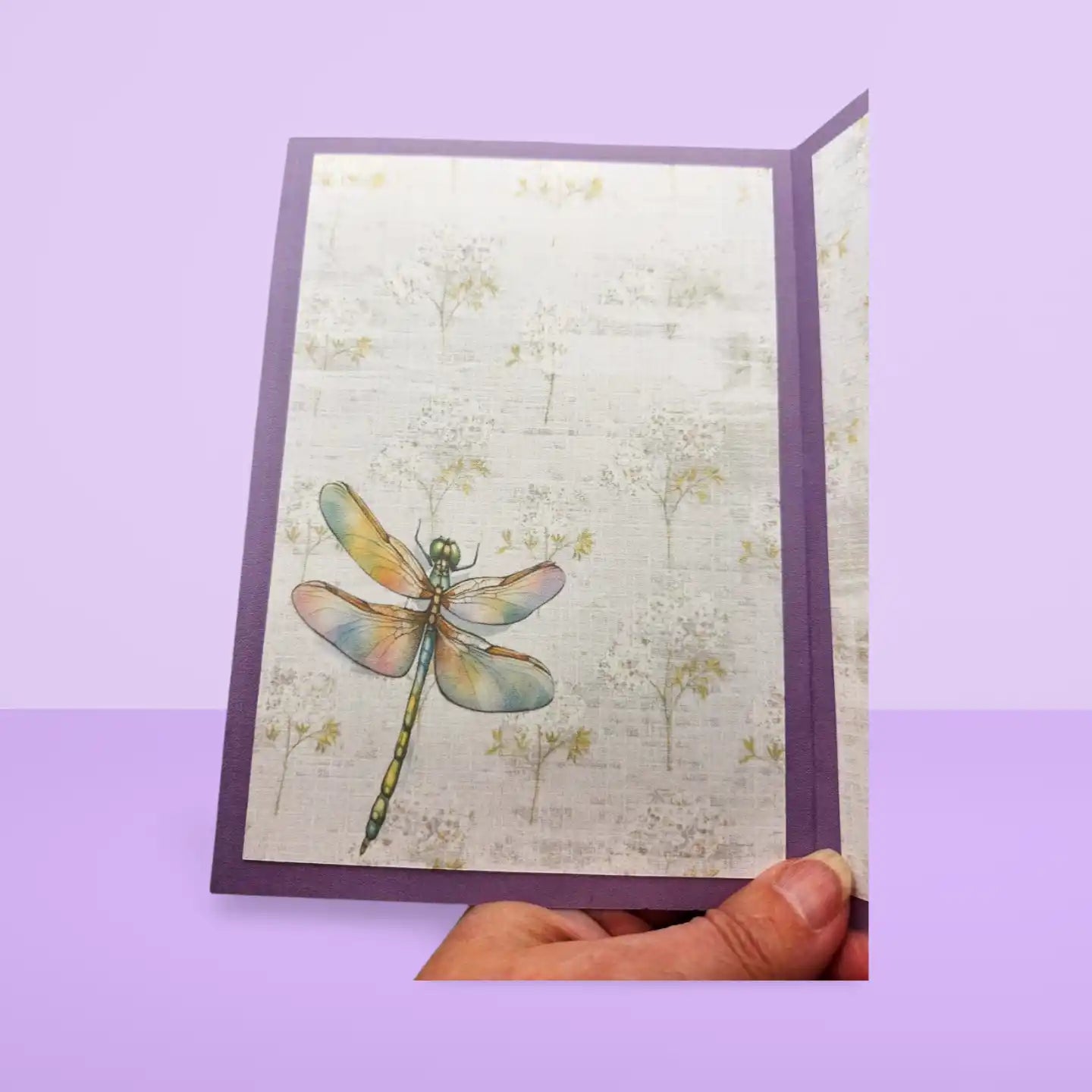 Greeting card with a dragonfly design held against a purple background