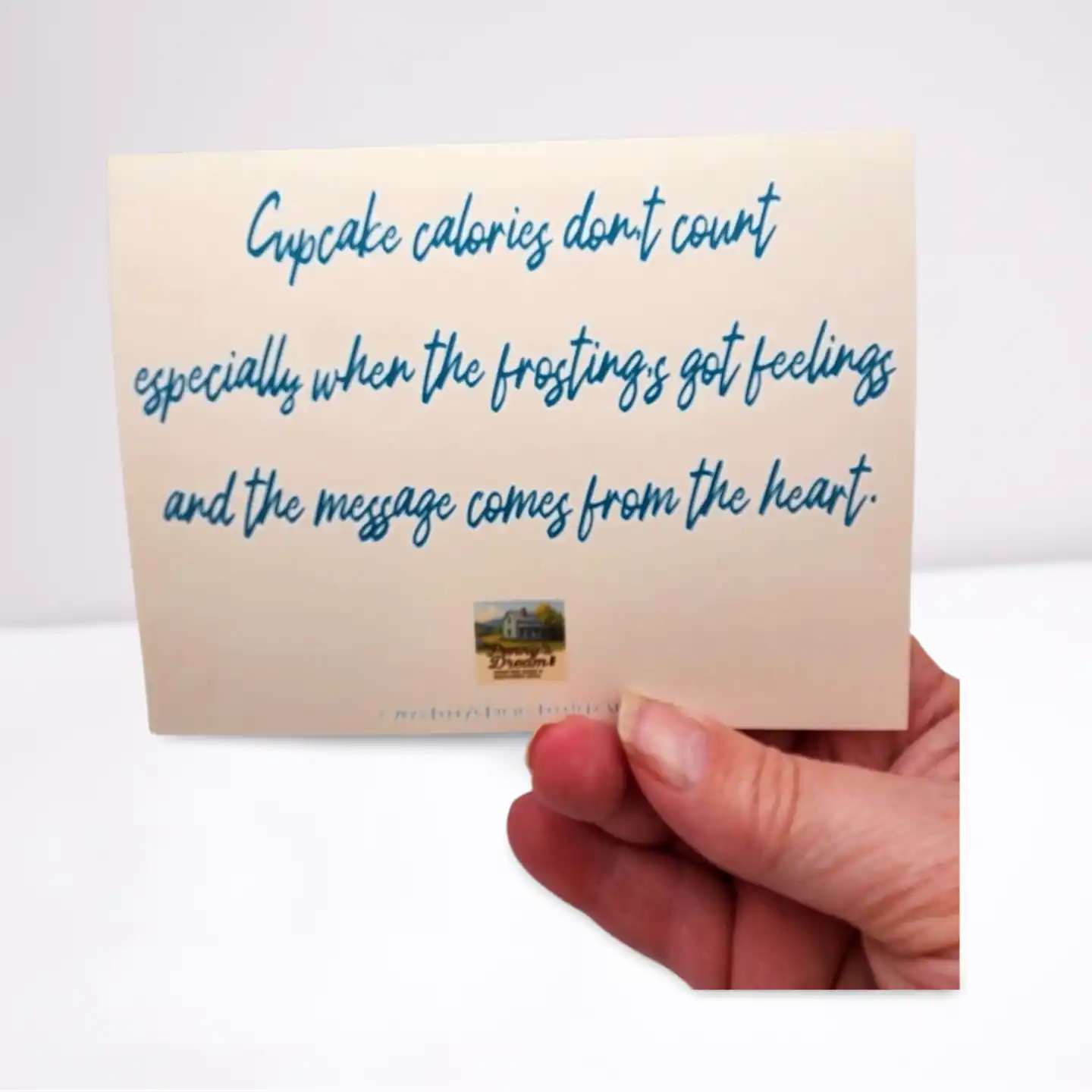 Hand holding a card with a humorous message about cupcake calories and frosting feelings.