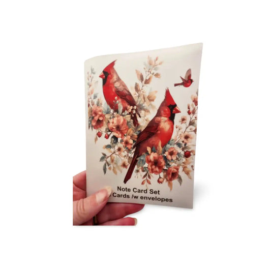 Note card set with red cardinals and flowers held by a hand on a white background