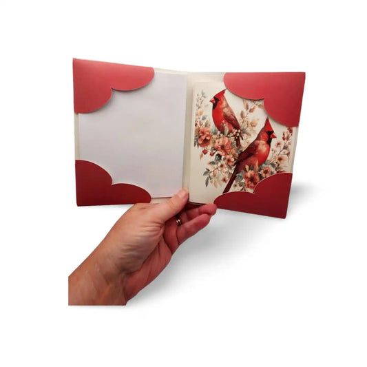 Hand holding a card with red cardinals and floral design on a white background