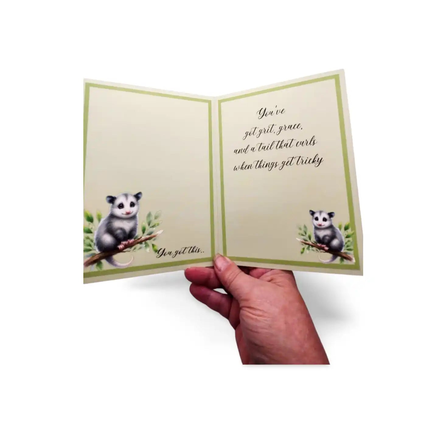 Hand holding a greeting card with an opossum illustration and text on a white background