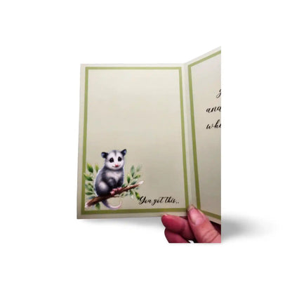 Card with an opossum illustration and text 'You got this' held by a hand.