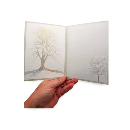 Hand holding a folded card with tree illustrations on a white background