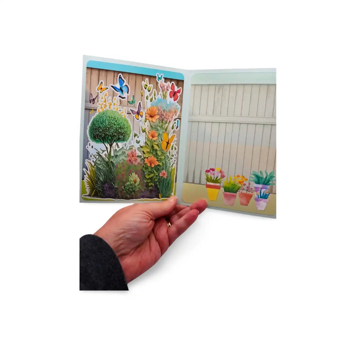 Hand holding a colorful garden scene with plants and butterflies on a white background