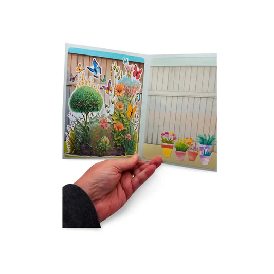 Hand holding a colorful garden scene with plants and butterflies on a white background