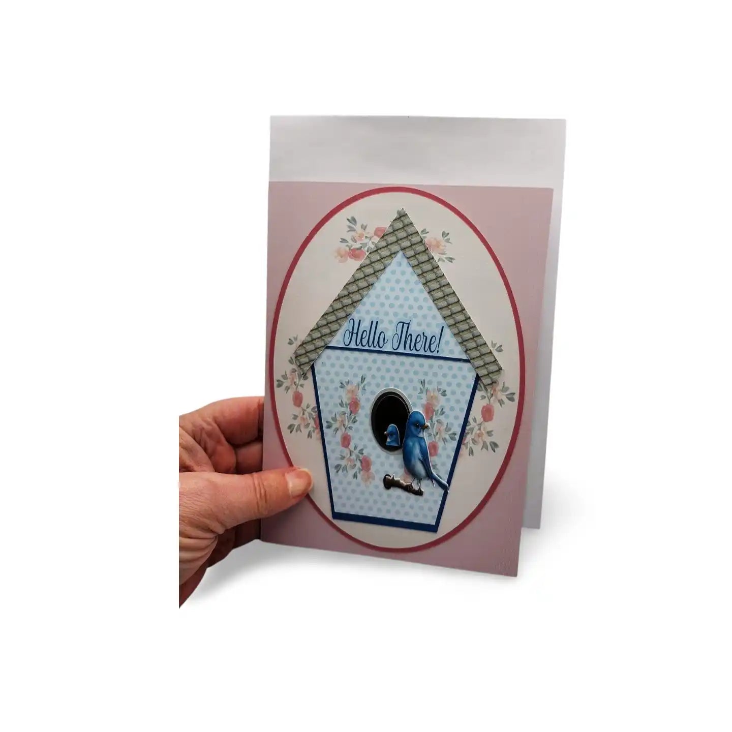 Greeting card with birdhouse design and 'Hello There!' text, held by a hand on a white background
