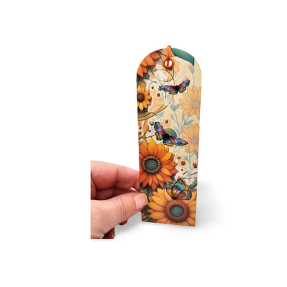 Decorative bookmark with sunflowers and butterflies held by a hand on a white background