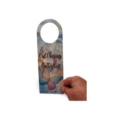 Decorative door hanger with butterfly design and text held by a hand on a white background