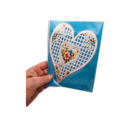 Hand holding a decorative card with heart designs and floral patterns on a blue background