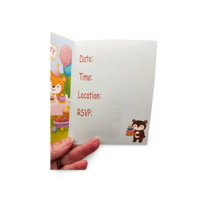 Hand holding a birthday invitation card with a cartoon character and space for details.