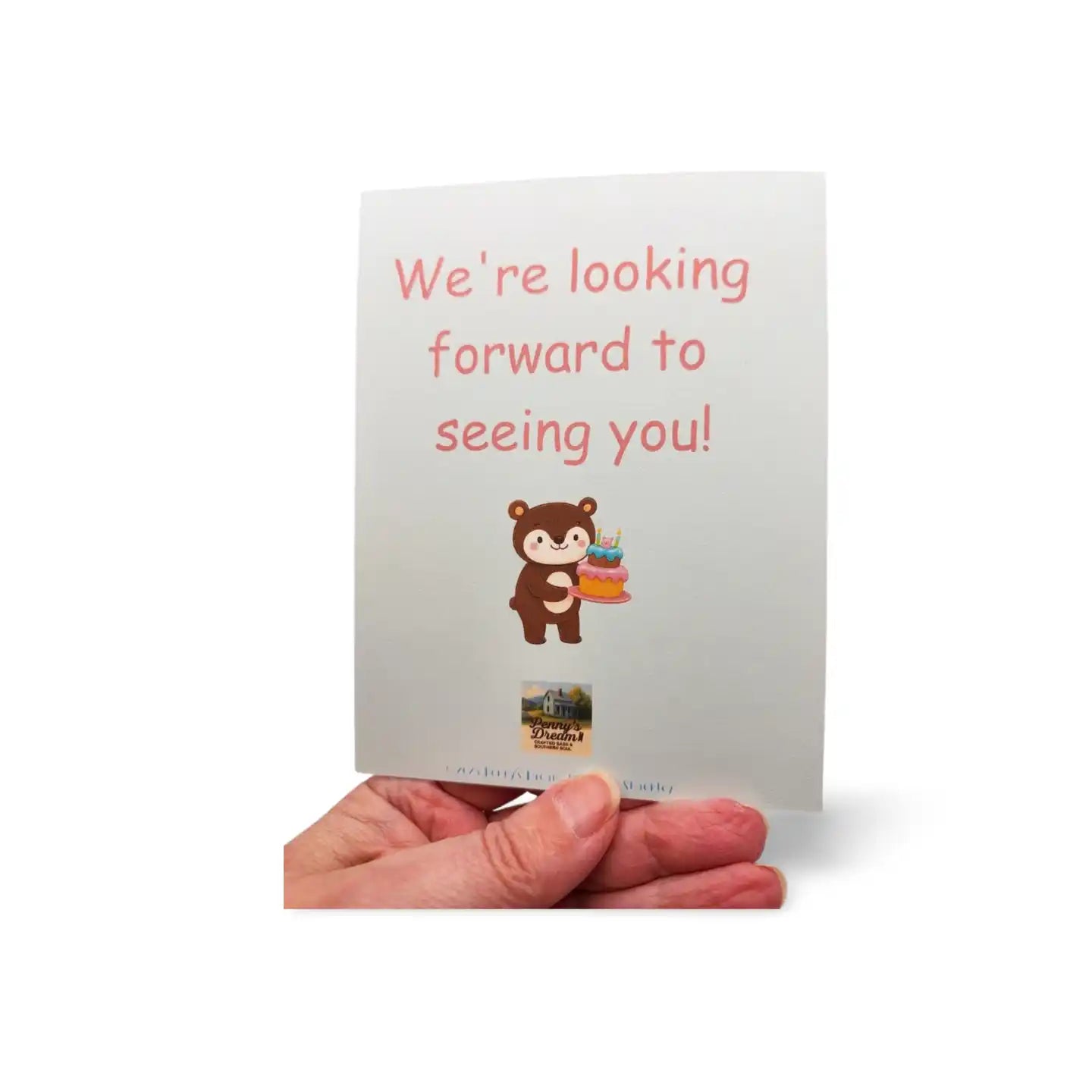 Hand holding a greeting card with a bear illustration and text on a white background