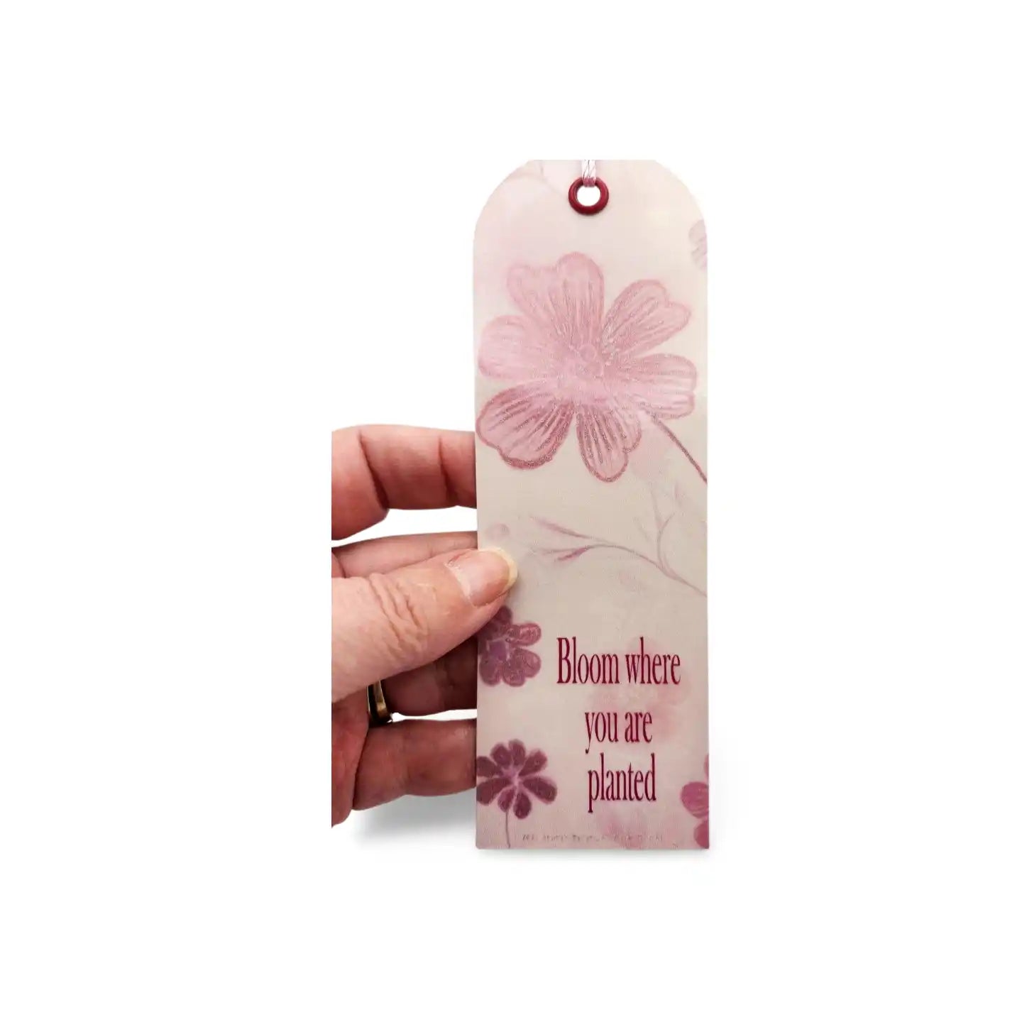 Floral bookmark with 'Bloom where you are planted' text held by a hand on a white background