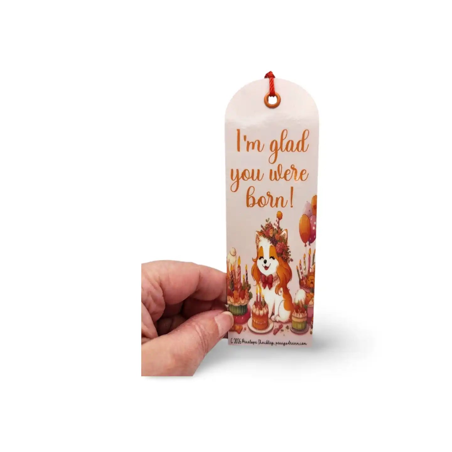 Hand holding a decorative bookmark with a dog illustration and text on a white background