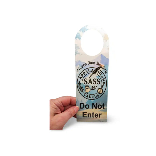 Hand holding a door hanger with 'Do Not Enter' text and mountain design