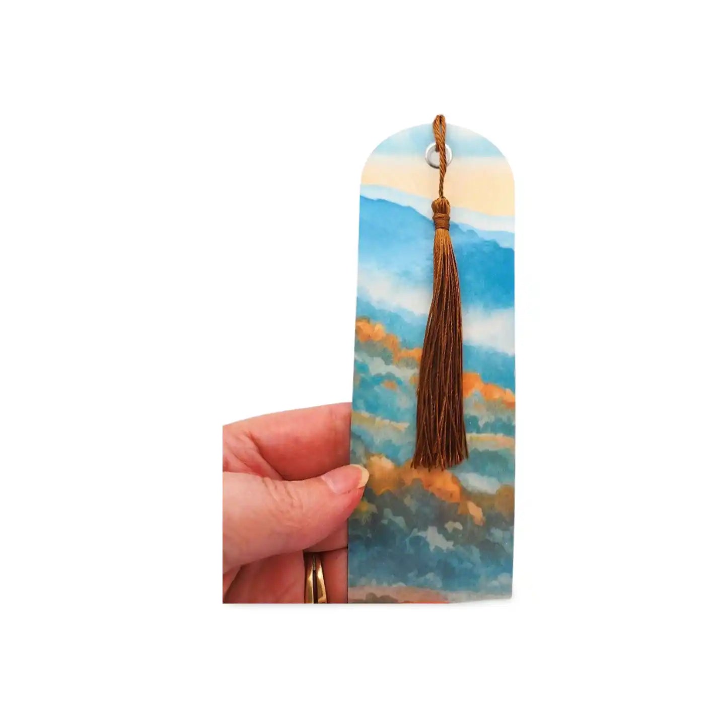 Bookmark with a scenic design and tassel held by a hand on a white background