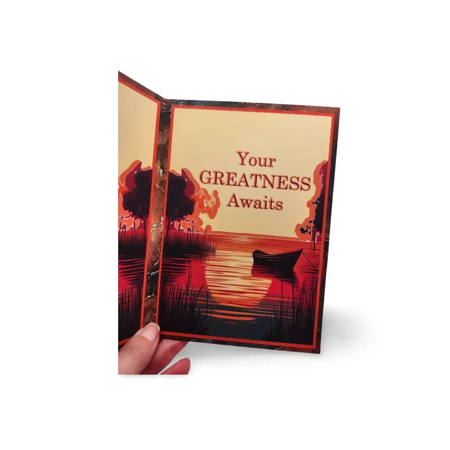 Card with a scenic design and 'Your GREATNESS Awaits' text, held open by a hand.