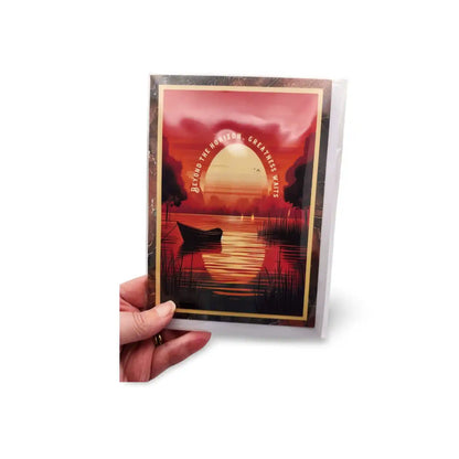 Hand holding a card with a sunset design and silhouette of a boat.