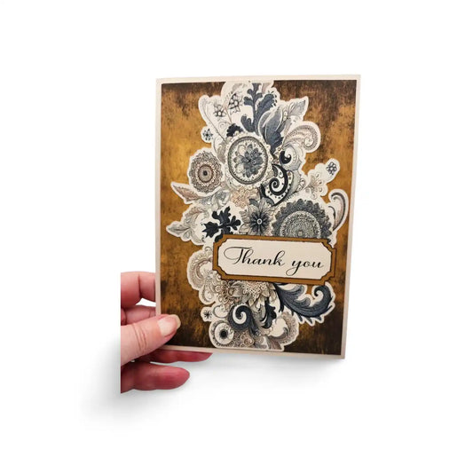 Decorative card with floral patterns and 'Thank you' text held by a hand on a white background