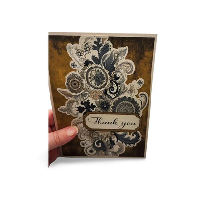 Decorative card with lace design and 'Thank you' text held by a hand on a white background