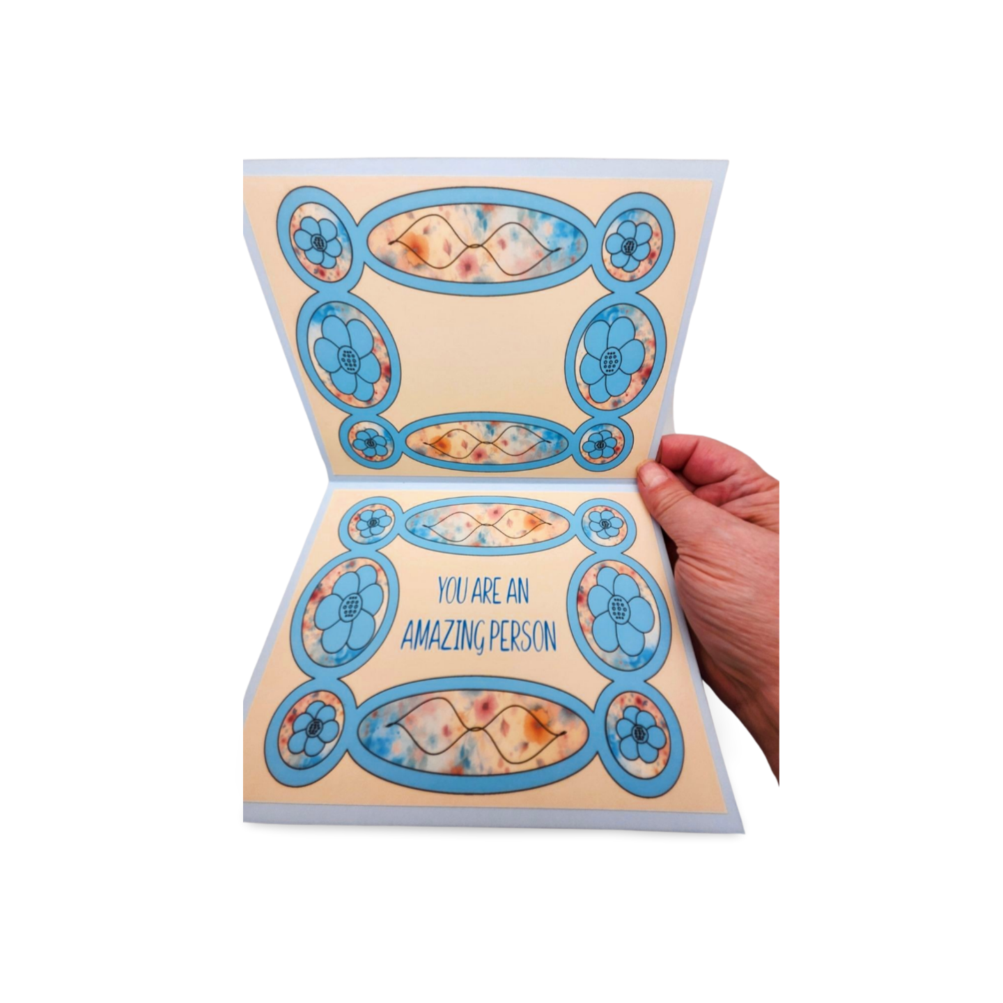 Hand holding a decorative card with floral designs and text on a white background