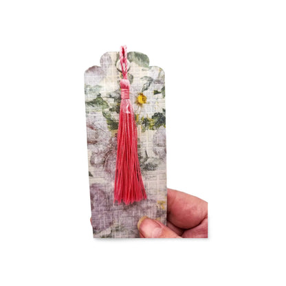 Floral bookmark with a pink tassel held by a hand on a white background