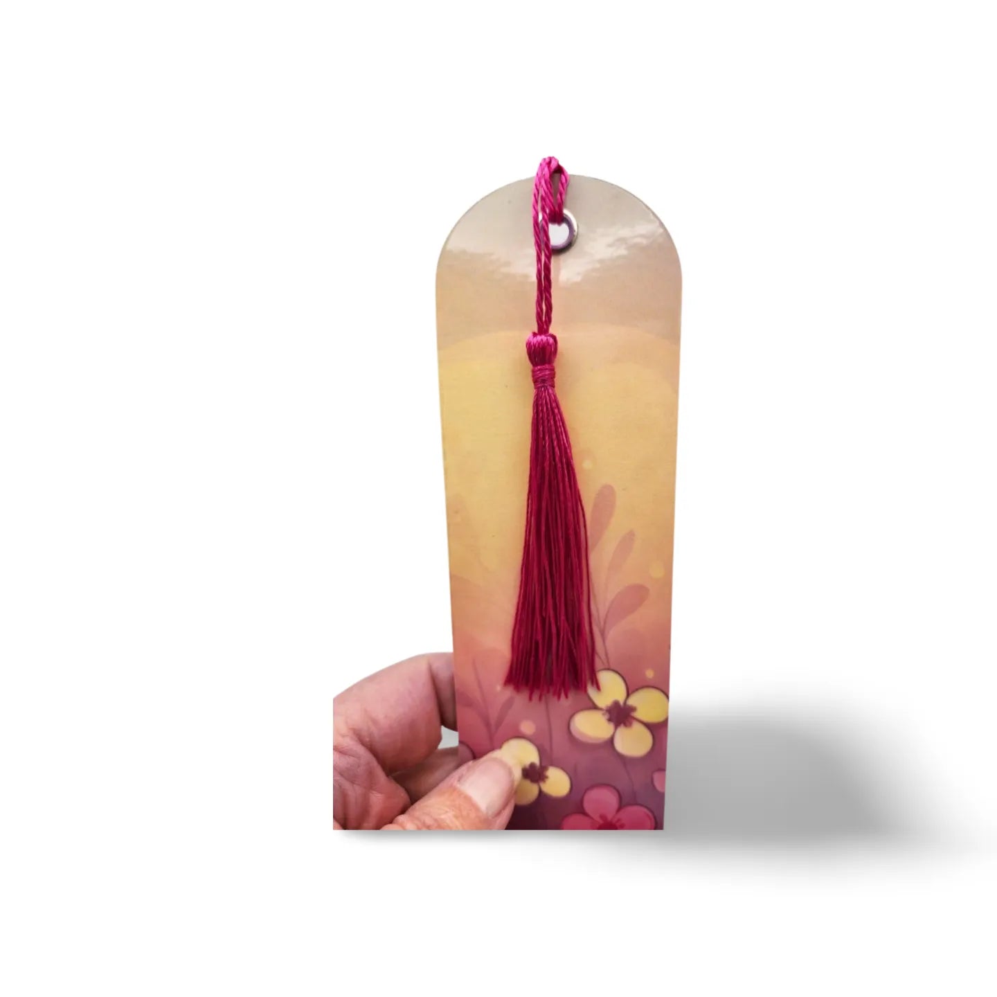 Decorative bookmark with floral design and red tassel held by a hand on a white background