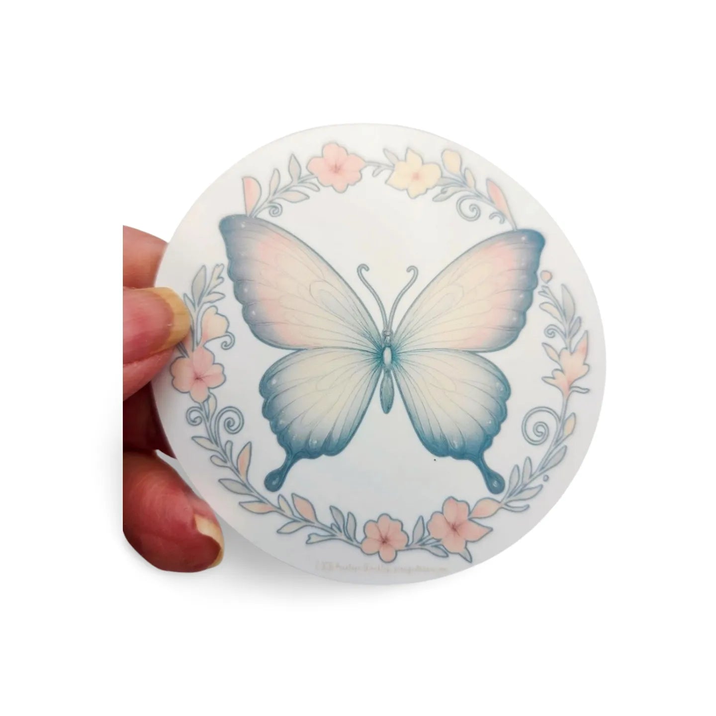 Round decorative item with a butterfly design held by a hand on a white background