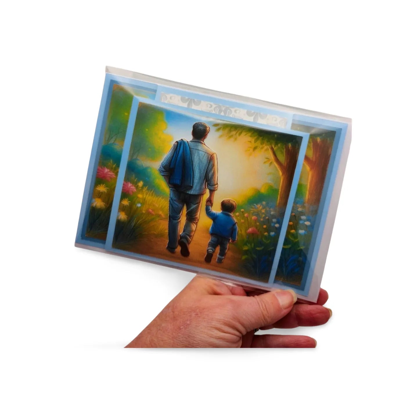 Hand holding a card with a painting of a man and child walking together in a garden.