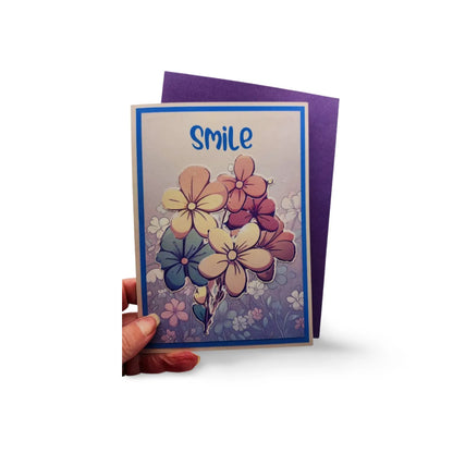 Greeting card with floral design and 'smile' text held by a hand on a white background