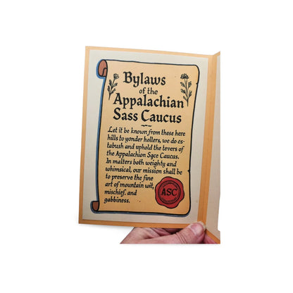Card with 'Bylaws of the Appalachian Sass Caucus' text and a hand holding it.