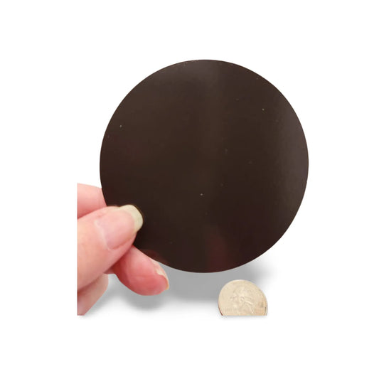 Hand holding a large black round object next to a small beige object on a white background